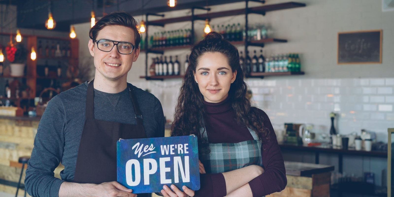 Pexels Photo by Vitaly Gariev Friendly café owners holding an 'Open' sign welcoming customers into their modern coffee shop.