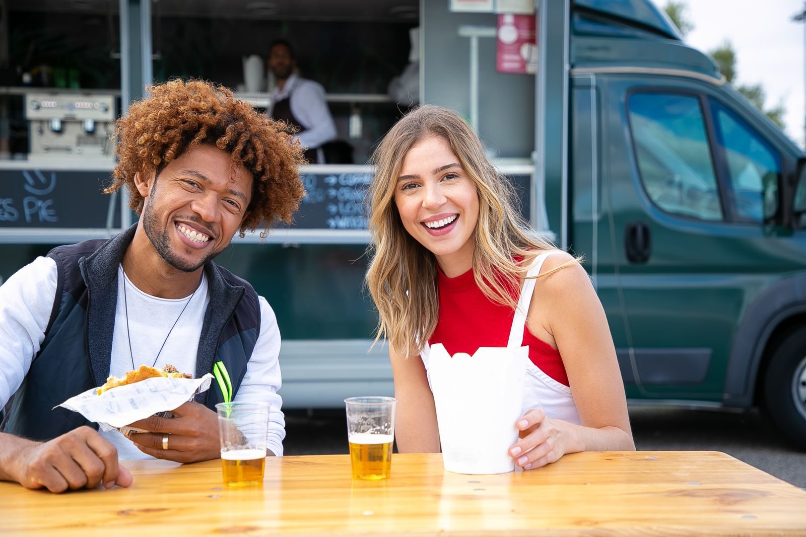 Pexels Photo by Kampus Production Cheerful young lady with African American male friend smiling and looking at camera while sitting at table in street cafe and eating burger with french fries and drinking beer