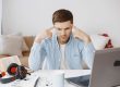 Focused man works at home office desk with laptop, documents, and headphones.