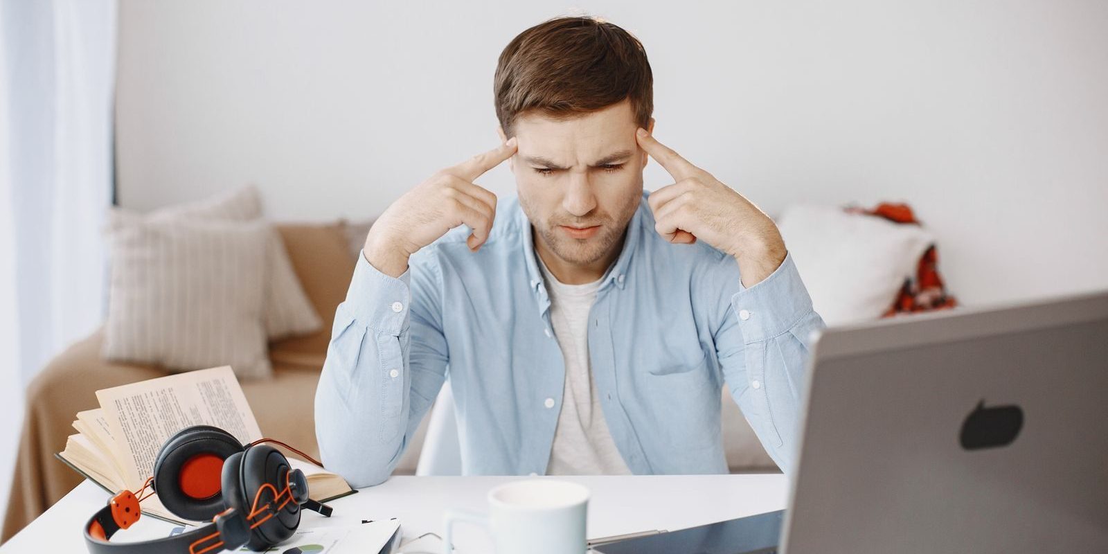 Focused man works at home office desk with laptop, documents, and headphones.