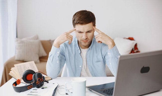 Focused man works at home office desk with laptop, documents, and headphones.