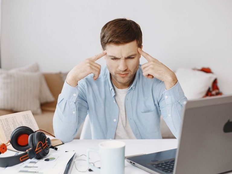 Focused man works at home office desk with laptop, documents, and headphones.