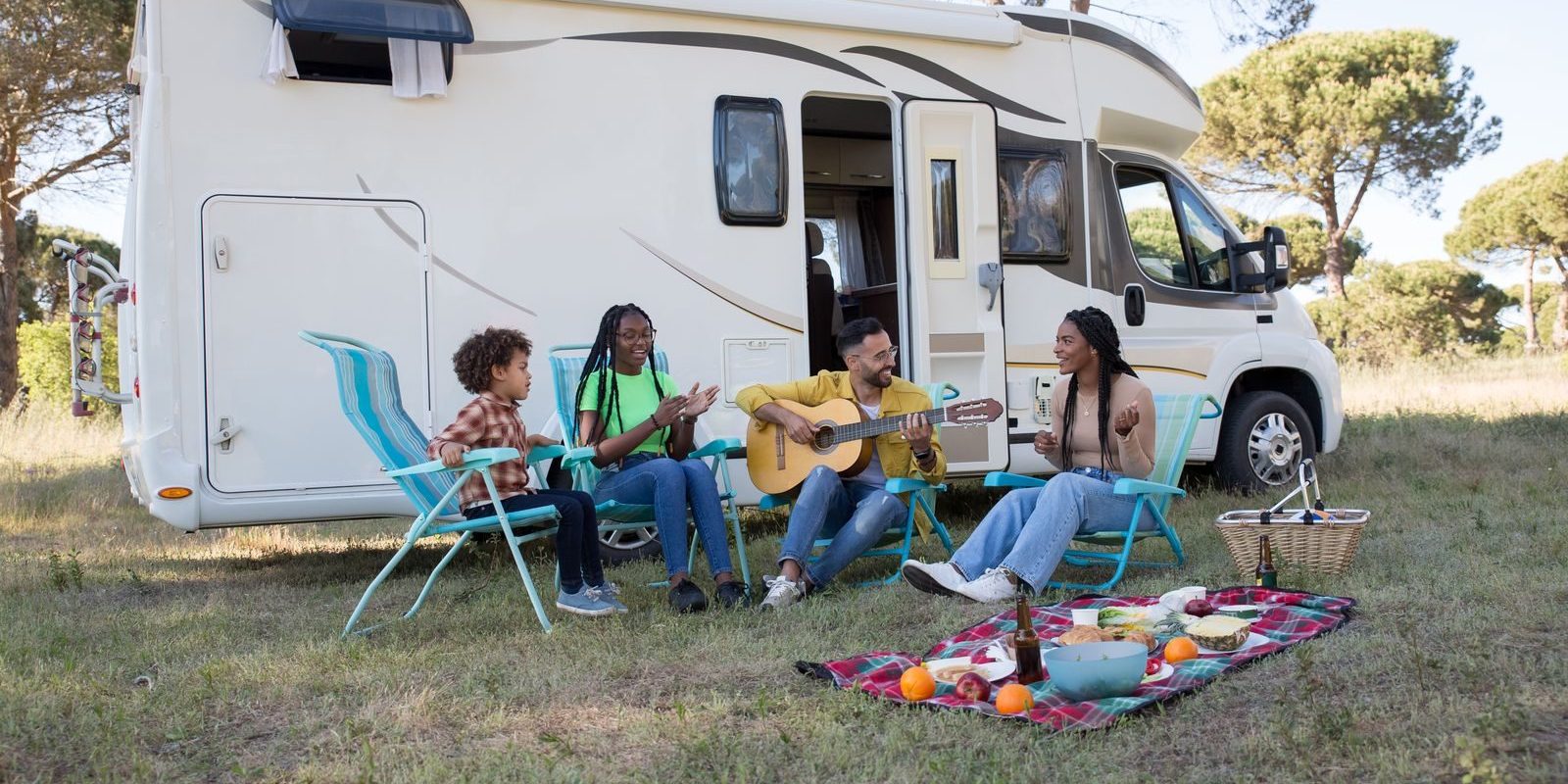 A family relaxing outdoors with a picnic and guitar by their camper, enjoying a sunny summer day in Portugal.