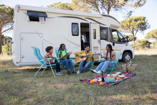 A family relaxing outdoors with a picnic and guitar by their camper, enjoying a sunny summer day in Portugal.
