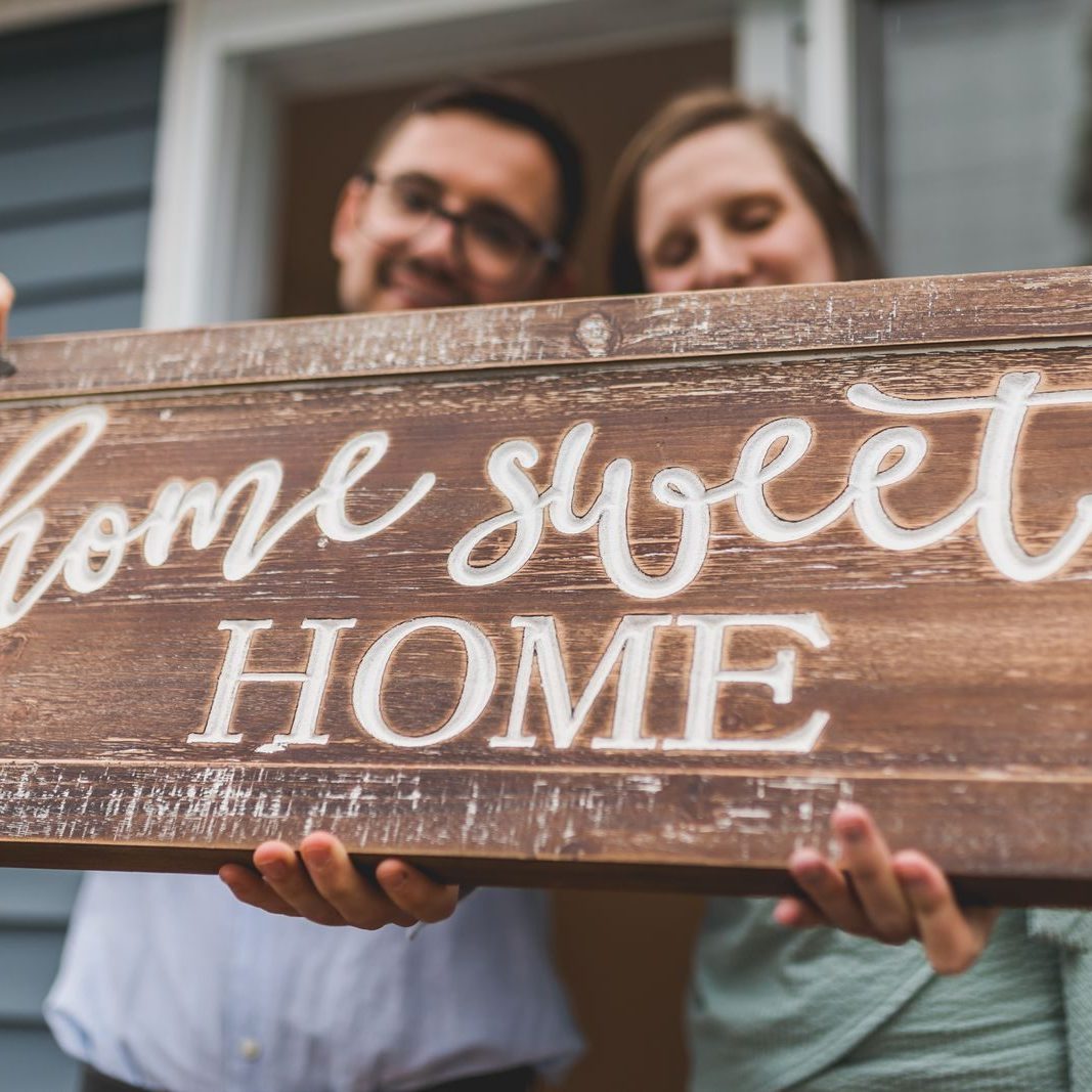 Pexels Photo by RDNE Stock project A joyful couple holding a 'home sweet home' sign in front of their new house.