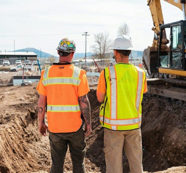 men in safety vests standing in front of a construction vehicle